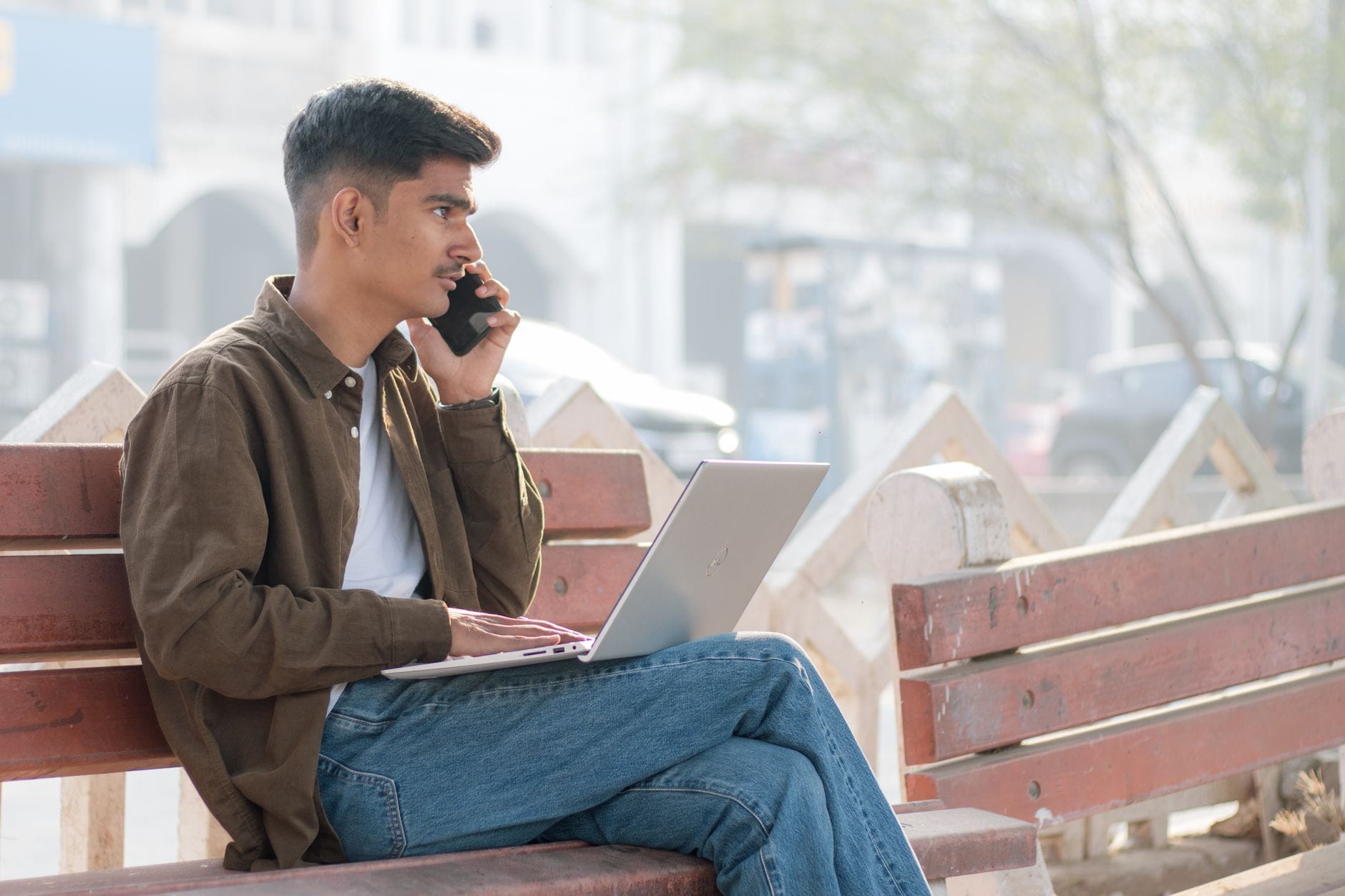 Freelancer z laptopem i telefonem pracuje zdalnie na ławce w parku
