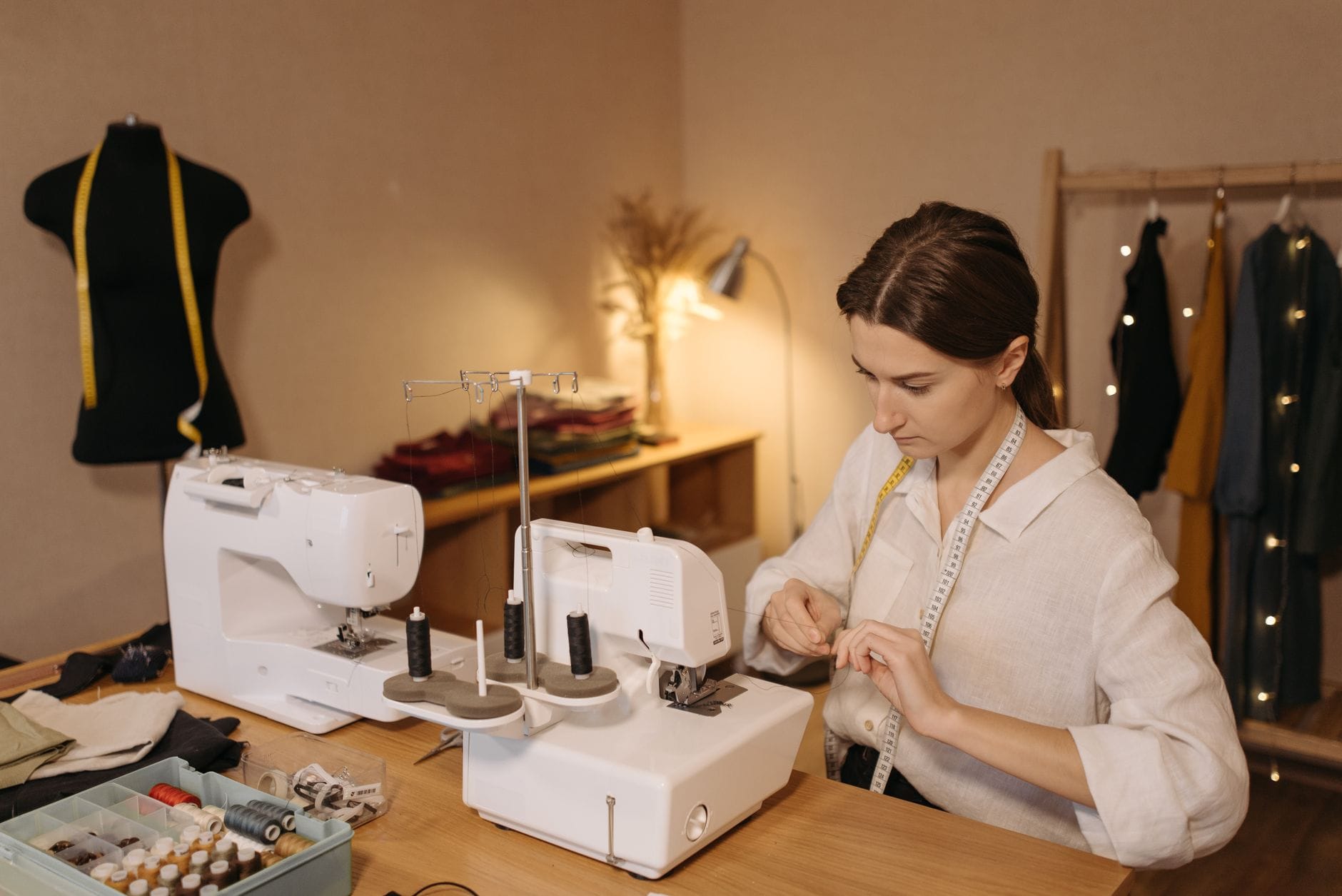 Kaukaska kobieta nawleka nić w maszynie do szycia w pracowni krawieckiej