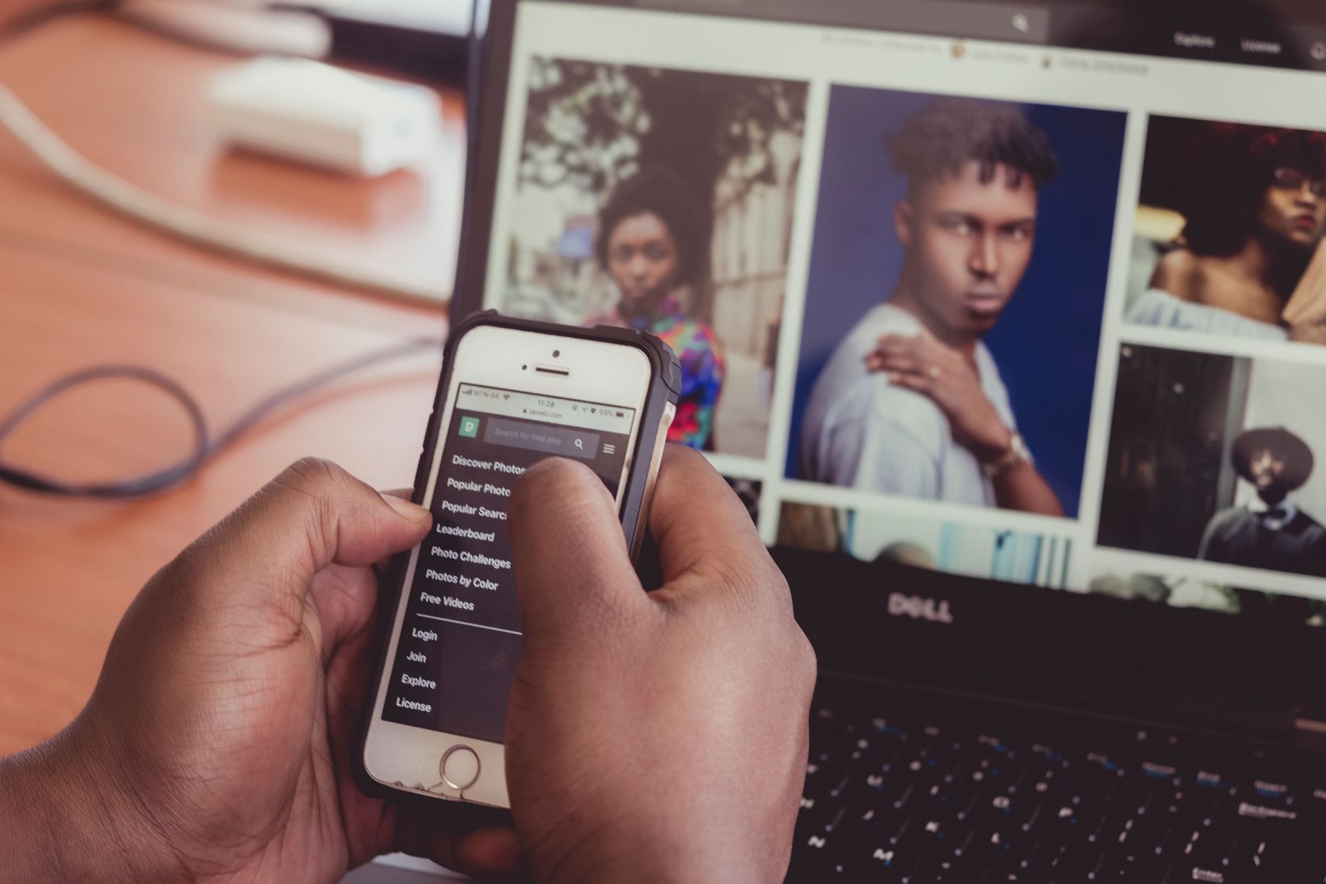 Dłonie z telefonem przed laptopem z podglądem grafik do social mediów Dłonie z telefonem przed laptopem z podglądem grafik do social mediów